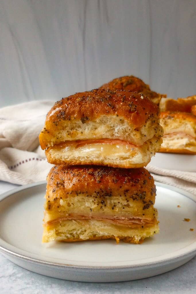 Picture of glazed ham and cheese sliders on a white plate with a towel in the background. 