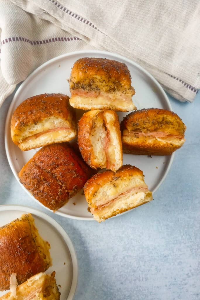 Overhead picture of ham and cheese sliders on a white plate. Rolls are arranged on their sides to show the middle. 