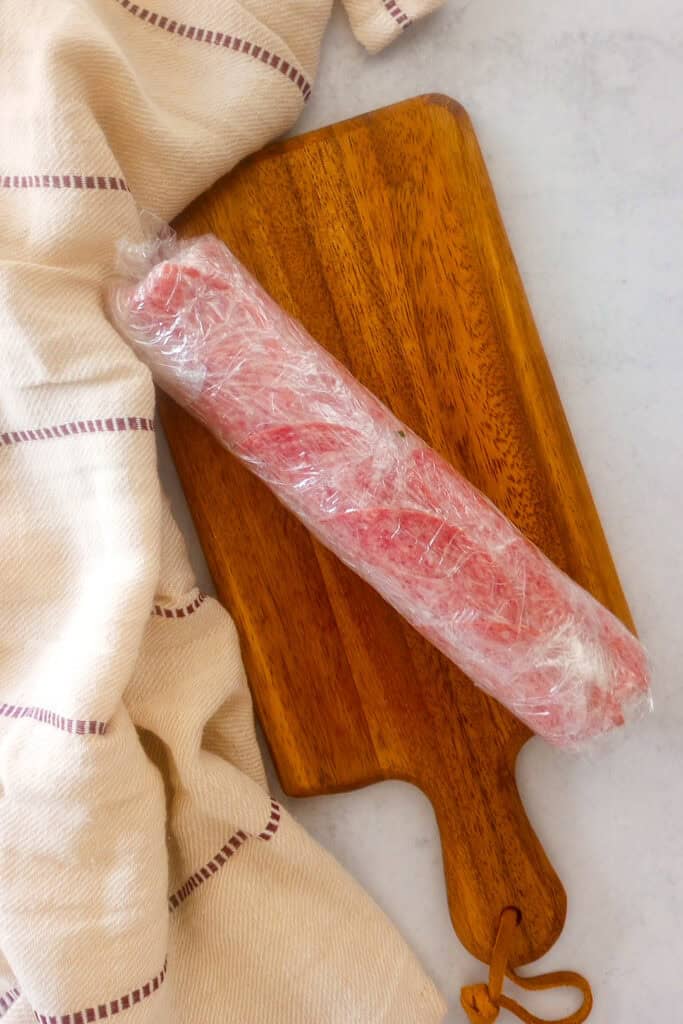 Picture of salami log rolled tightly in plastic wrap. 