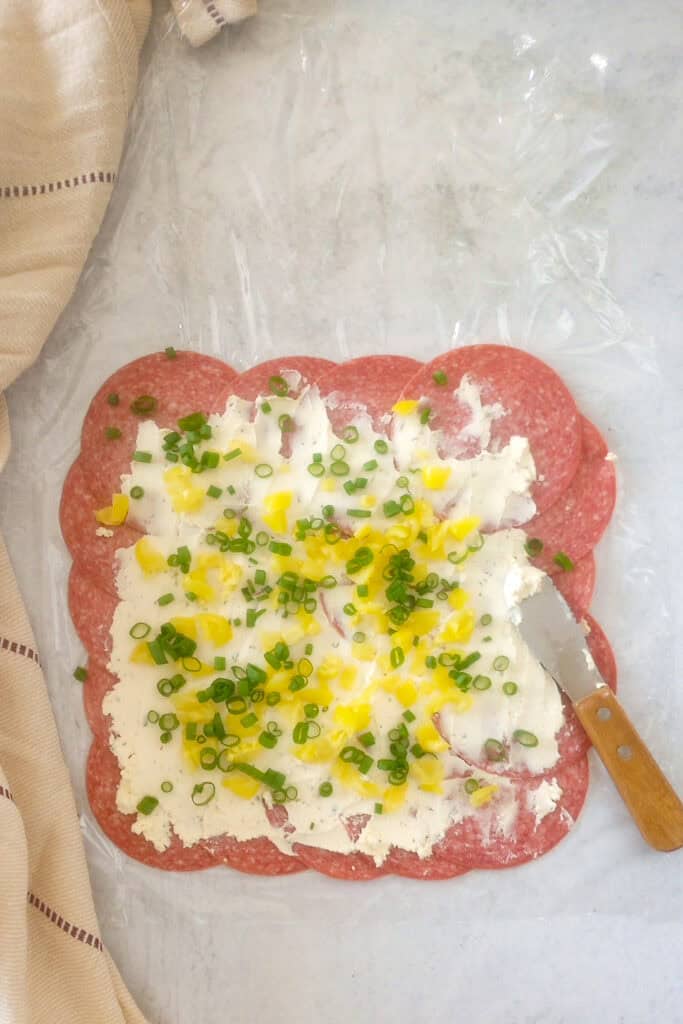 Overhead picture of salami with cheese spread evenly over-top and banana peppers and green onions sprinkled evenly throughout. 