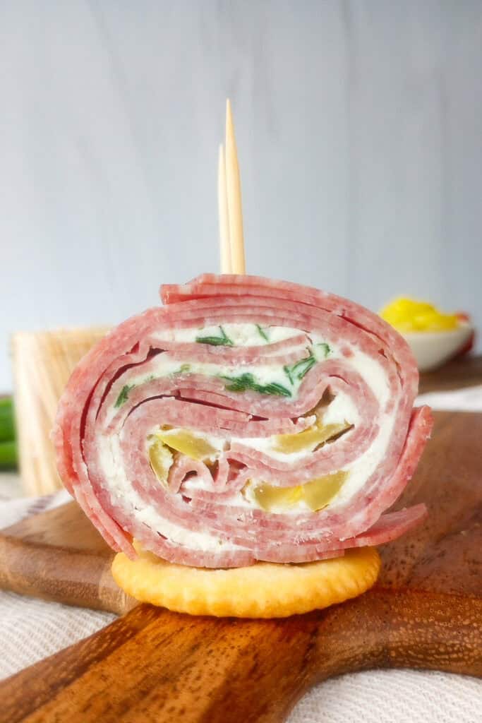 Up close picture of salami pinwheels on a cracker with a toothpick stuck in the top. 