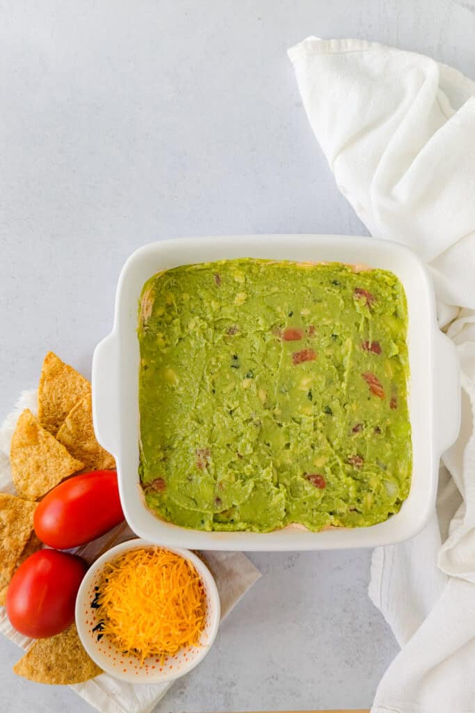 Overhead picture of guacamole spread evenly over refried beans and sour cream. 