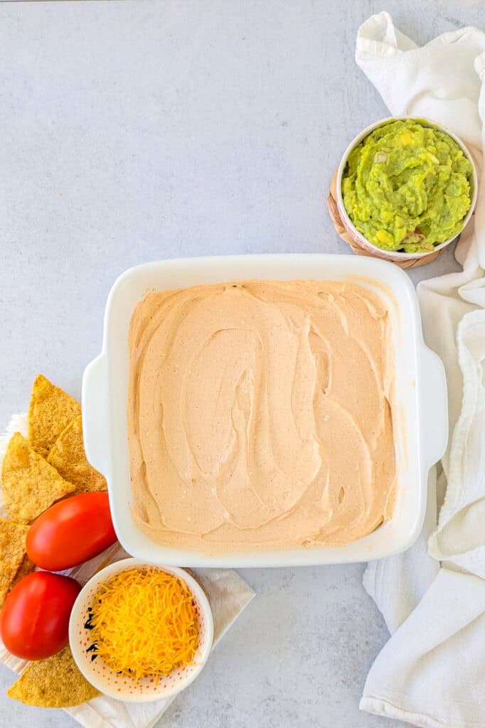 Overhead picture of refried beans in a baking dish topped with cream cheese and sour cream mixture. 