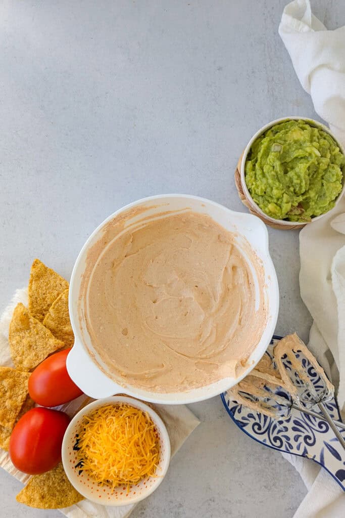 Overhead picture of cream cheese and sour cream seasoned with taco seasoning and arranged next to other ingredients. 