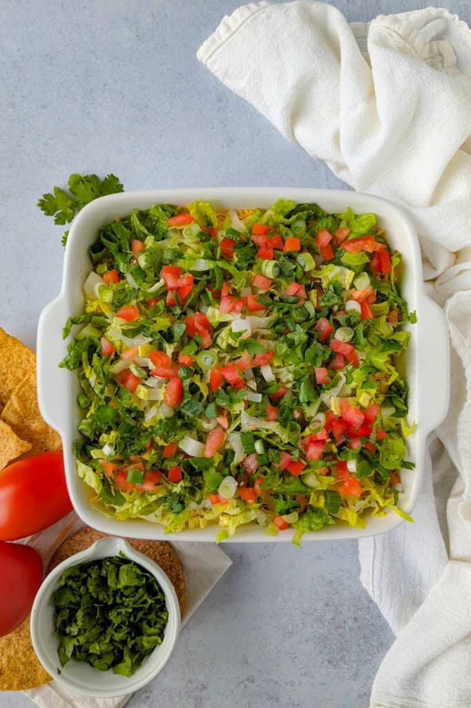 Overhead picture of layered taco dip topped with diced tomatoes, green onions, and cilantro. 