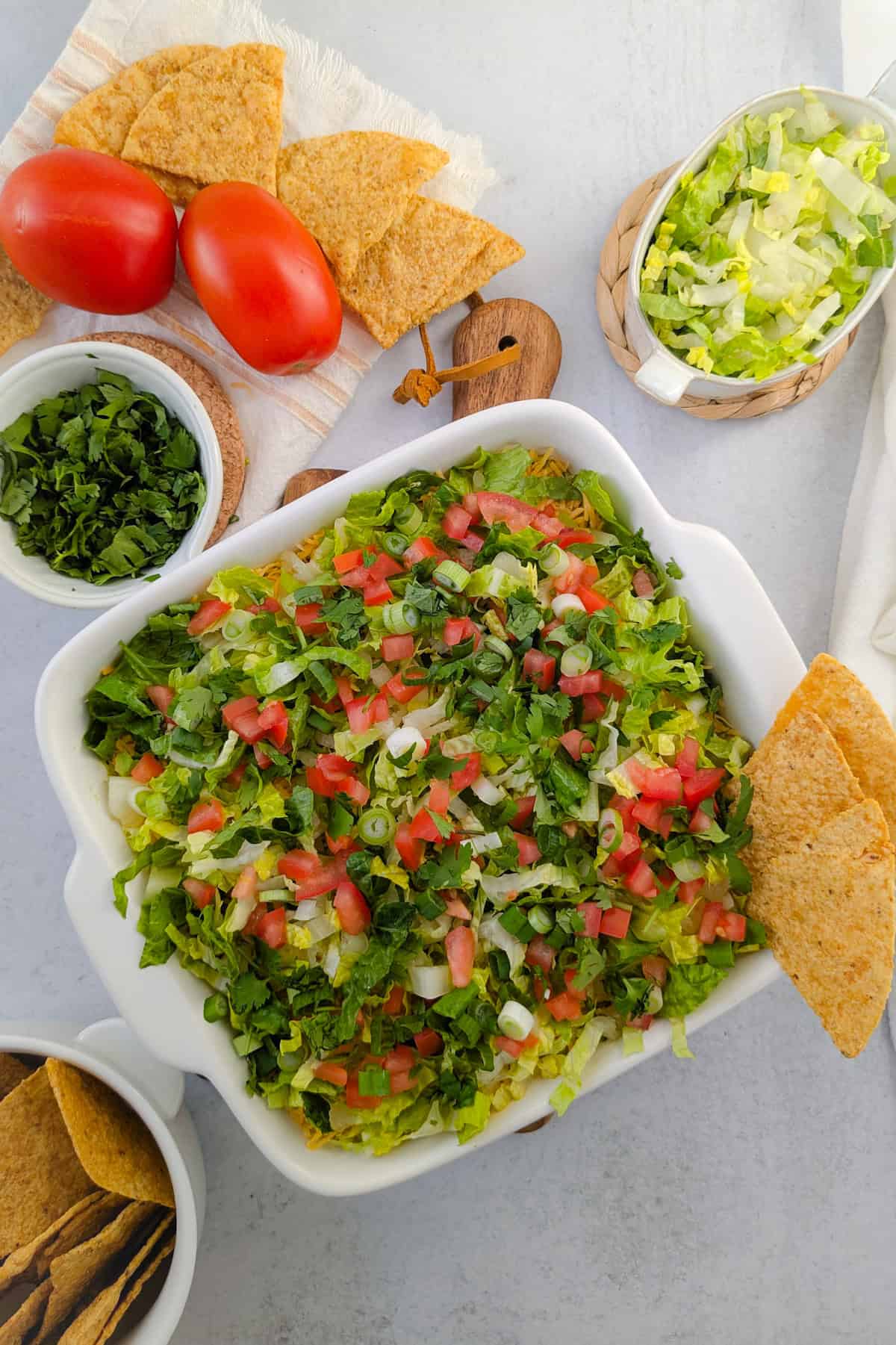 Overhead picture of taco dip next to shredded lettuce, diced tomatoes, chopped cilantro and tortilla chips.