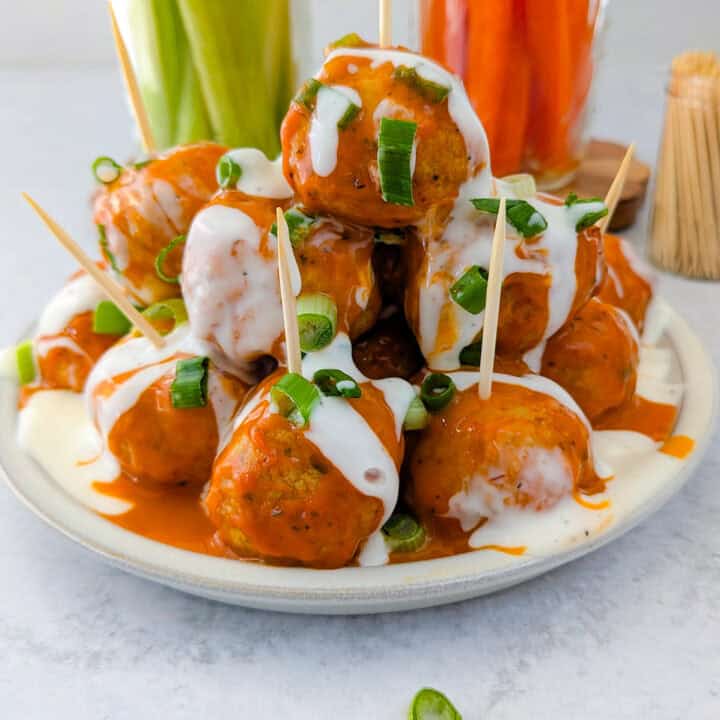 Buffalo chicken meatballs on a plate slathered with buffalo sauce, ranch dressing and garnished with chives.