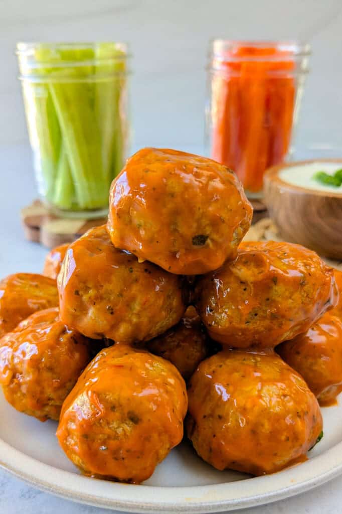 Picture of meatballs on a plate next to glass jars of celery and carrot sticks and a bowl of ranch dressing. 