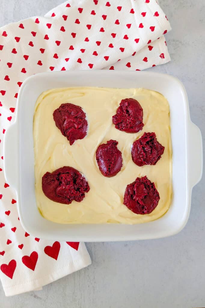 Overhead picture of reserved half a cup of brownie batter dolloped in spoonfuls over cheesecake batter.