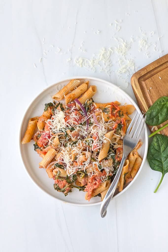 Overhead picture of baked Boursin cheese pasta on a white plate topped with grated Parmesan cheese.