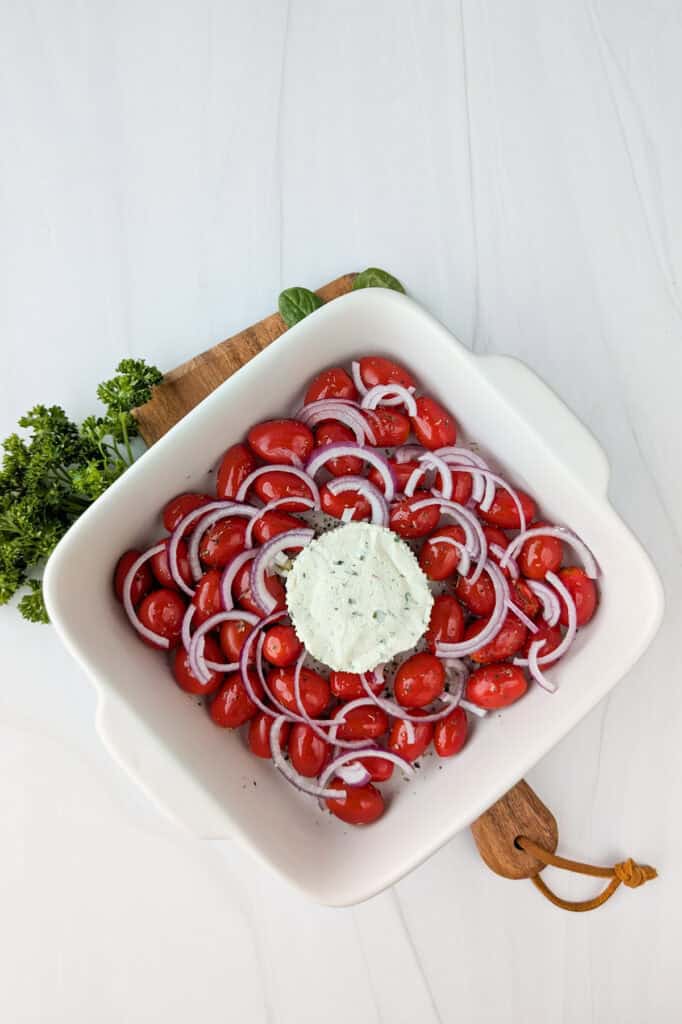 Overhead picture of grape tomatoes, sliced red onions and Boursin cheese in a baking dish.