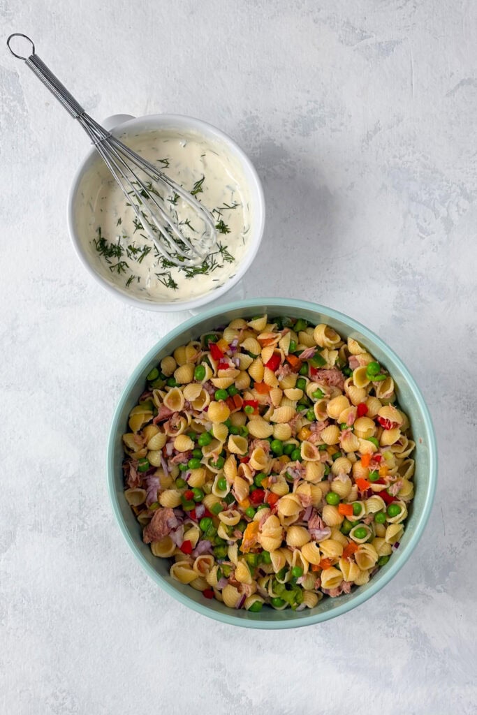 Overhead picture of dressing with a whisk bowl of pasta salad mixed up.