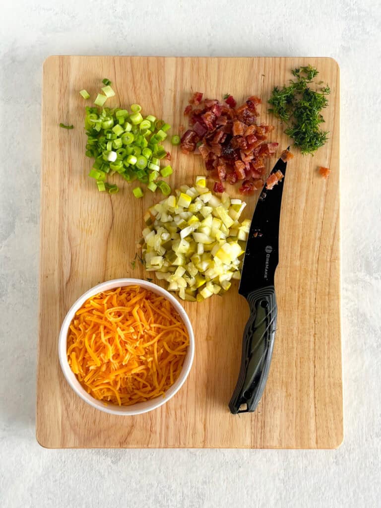 Overhead picture of chopped bacon, dill pickles, green onions, fresh dill, and shredded cheese.