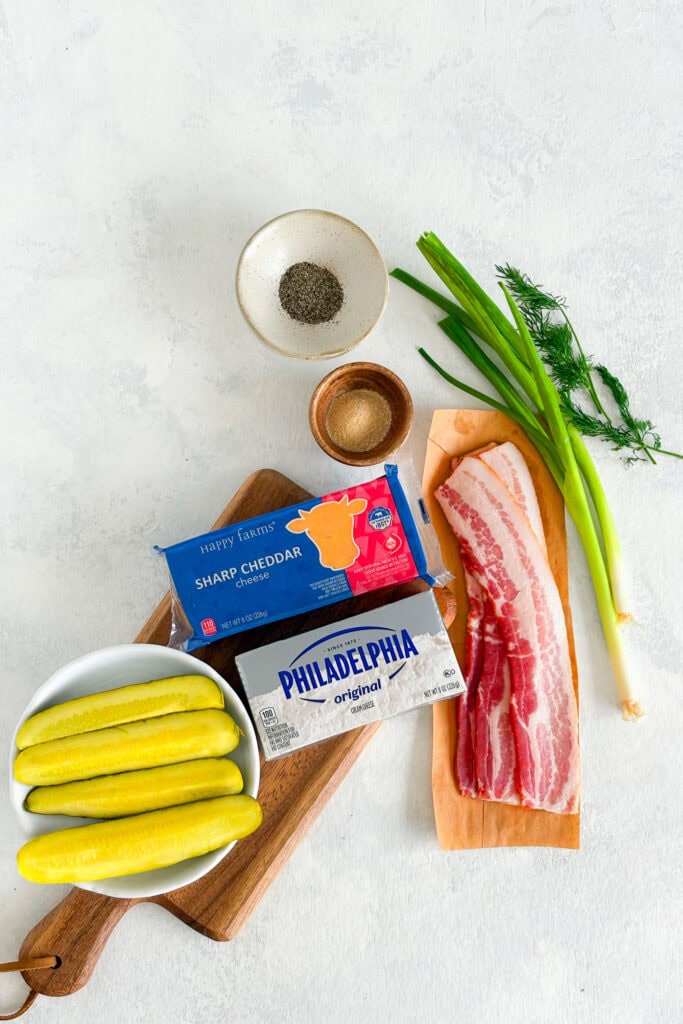 Overhead picture of ingredients needed to make Dill Pickle Fat Bombs. Bacon, sharp cheddar cheese, cream cheese, dill pickles, garlic powder, black pepper, and fresh dill.