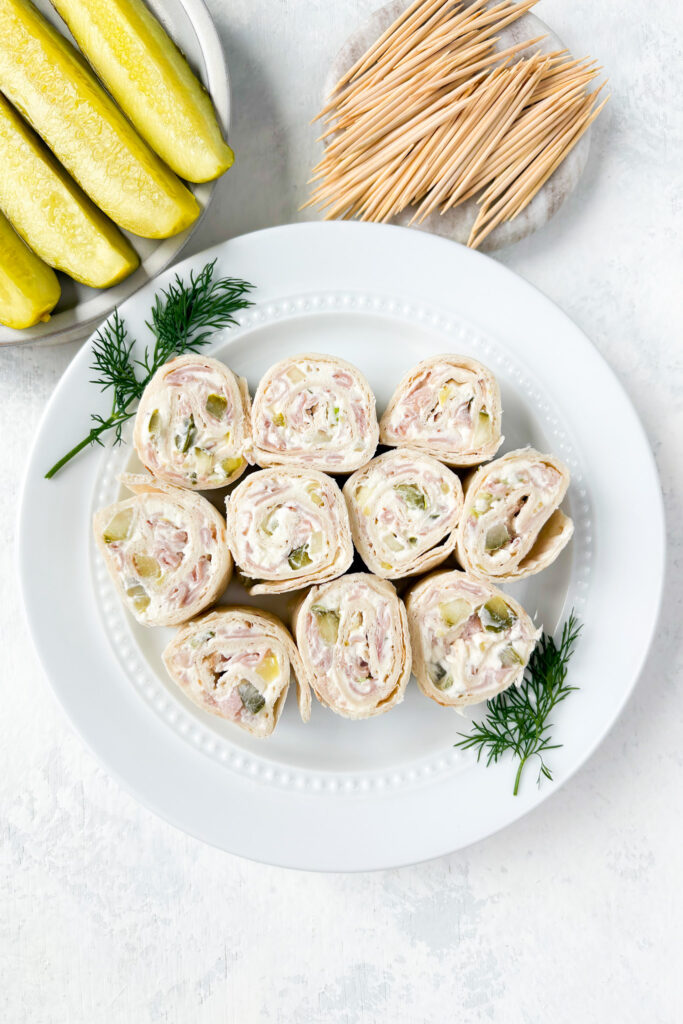 Overhead picture of pinwheels on a white plate next to fresh dill.