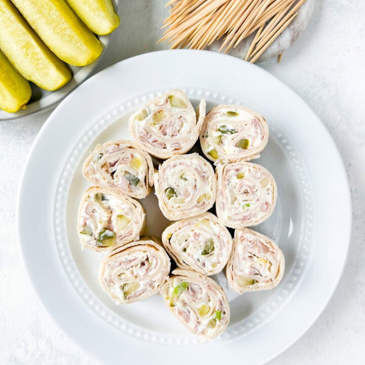 Overhead picture of pickle dip pinwheels on a white plate next to pickle spears and tooth picks.