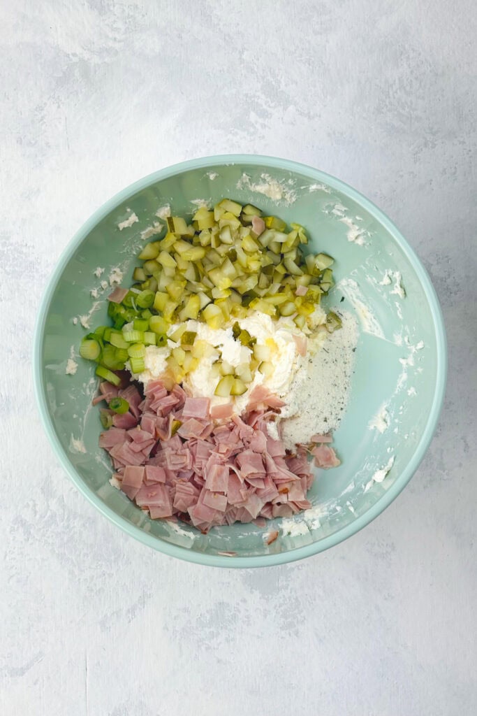 Overhead picture of diced ham and diced pickles ranch seasoning and cream cheese in a blue bowl.