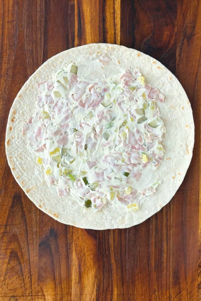 Overhead picture of cream cheese and pickle mix spread into a flour tortilla with about a 1/2 inch space around the edges.