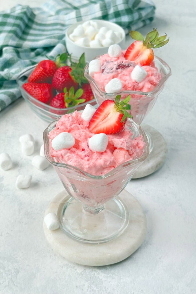 Two glass goblets filled with strawberry fluff salad that are garnished with a few mini marshmallows and a strawberry.